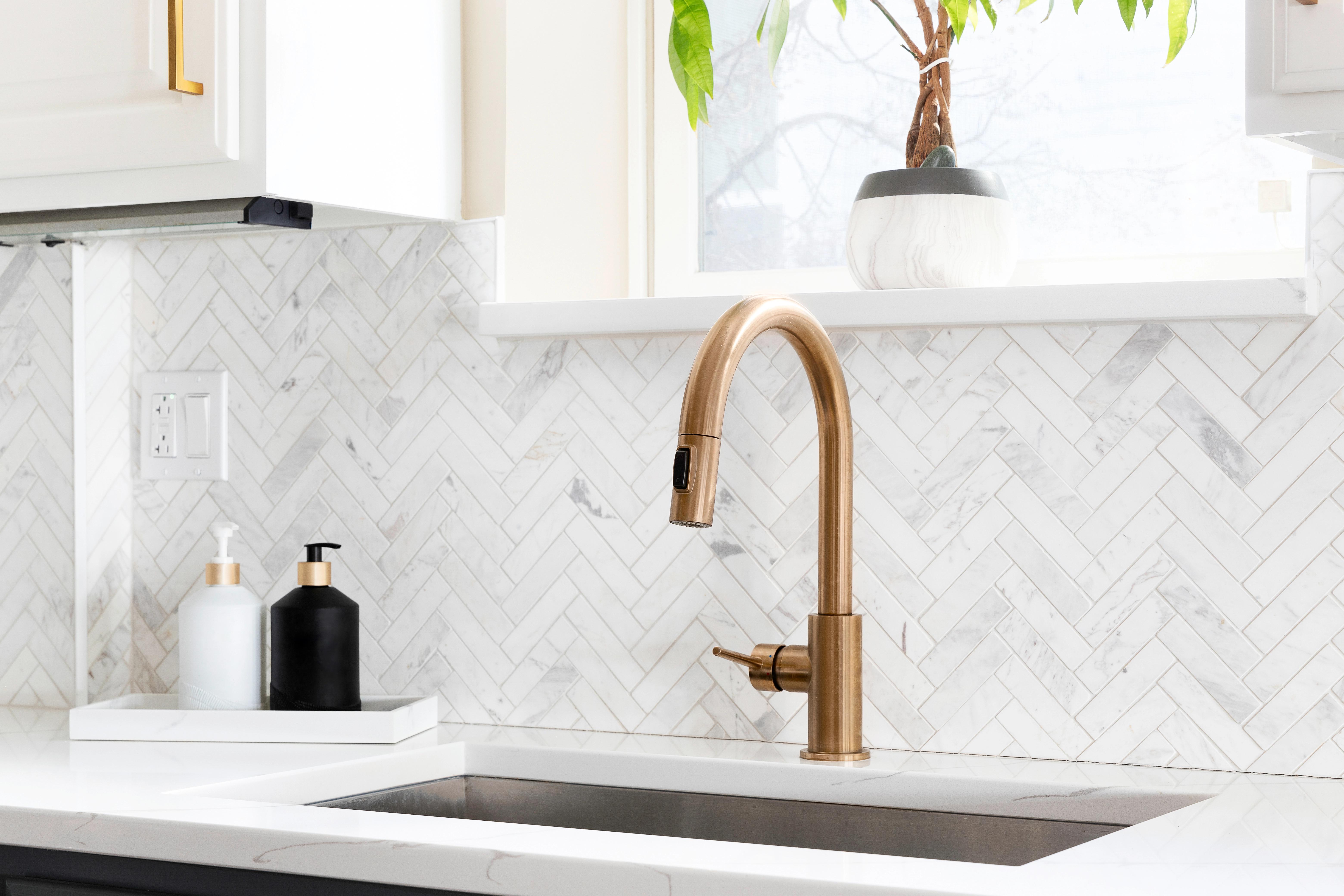 Modern kitchen with white marble herringbone tile backsplash and brushed gold faucet